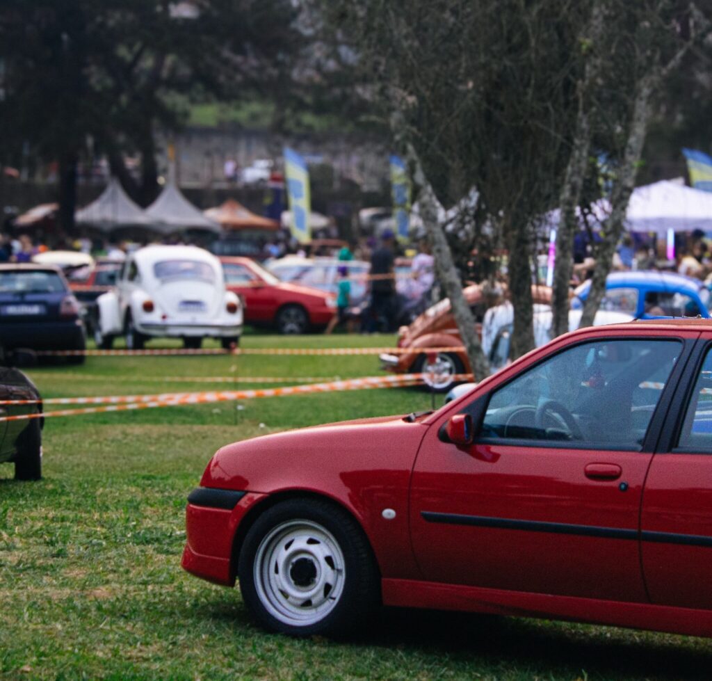 Colorful scene at a classic car show with a prominent red sports car and vintage vehicles.